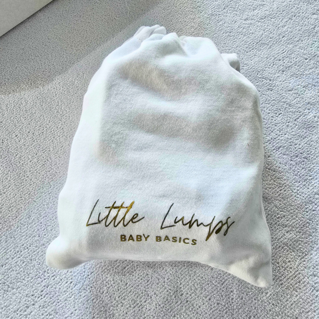 White drawstring bag with 'Little Lumps Baby Basics' text on a textured surface