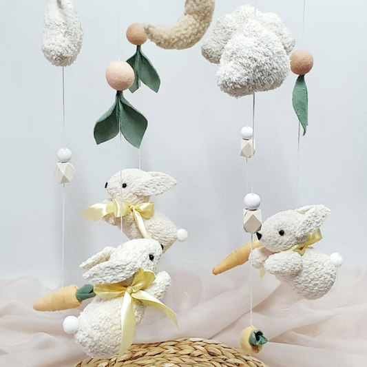 Baby mobile with cream boucle bunnies, carrots, and decorative elements on a light background