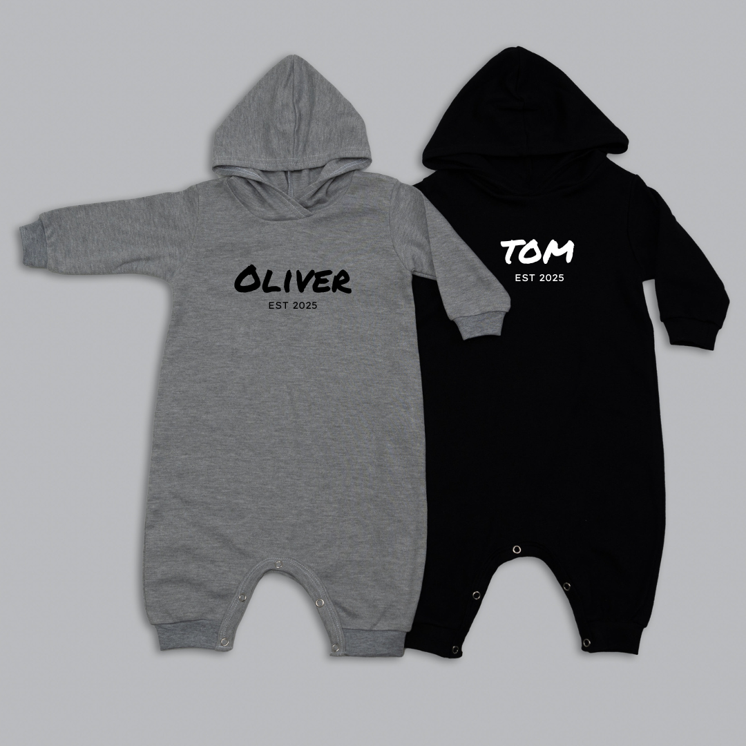 Two baby rompers, one gray and one black, with names printed on them against a light gray background.