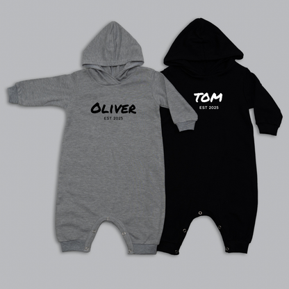 Two baby rompers, one gray and one black, with names printed on them against a light gray background.