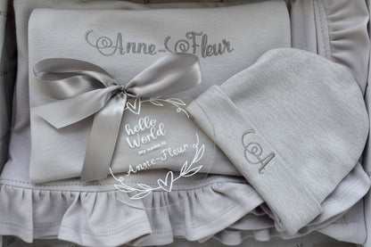 Pink baby outfit with a bow and embroidered text on a textured surface