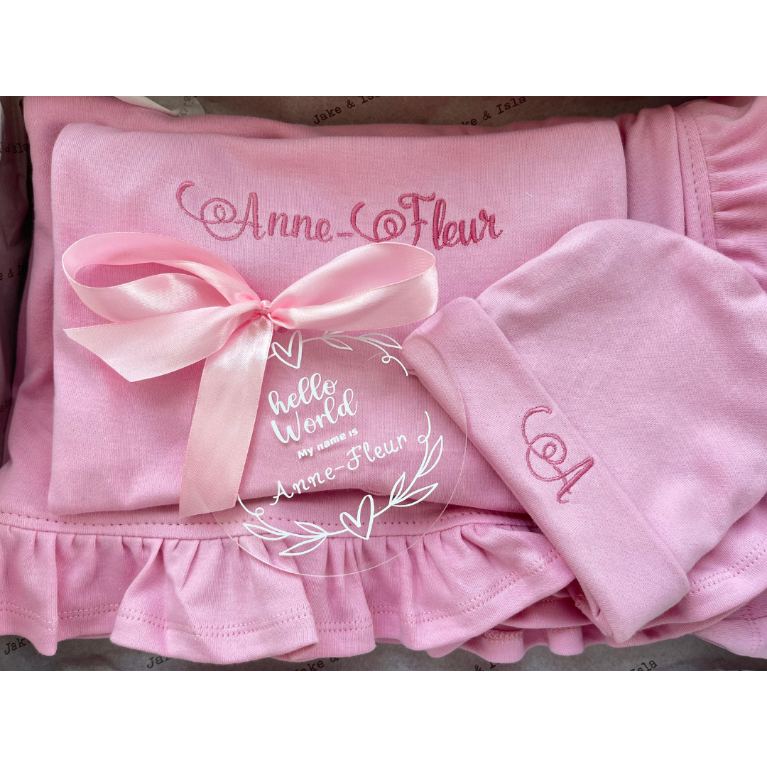 Pink baby outfit with a bow and embroidered text on a white background