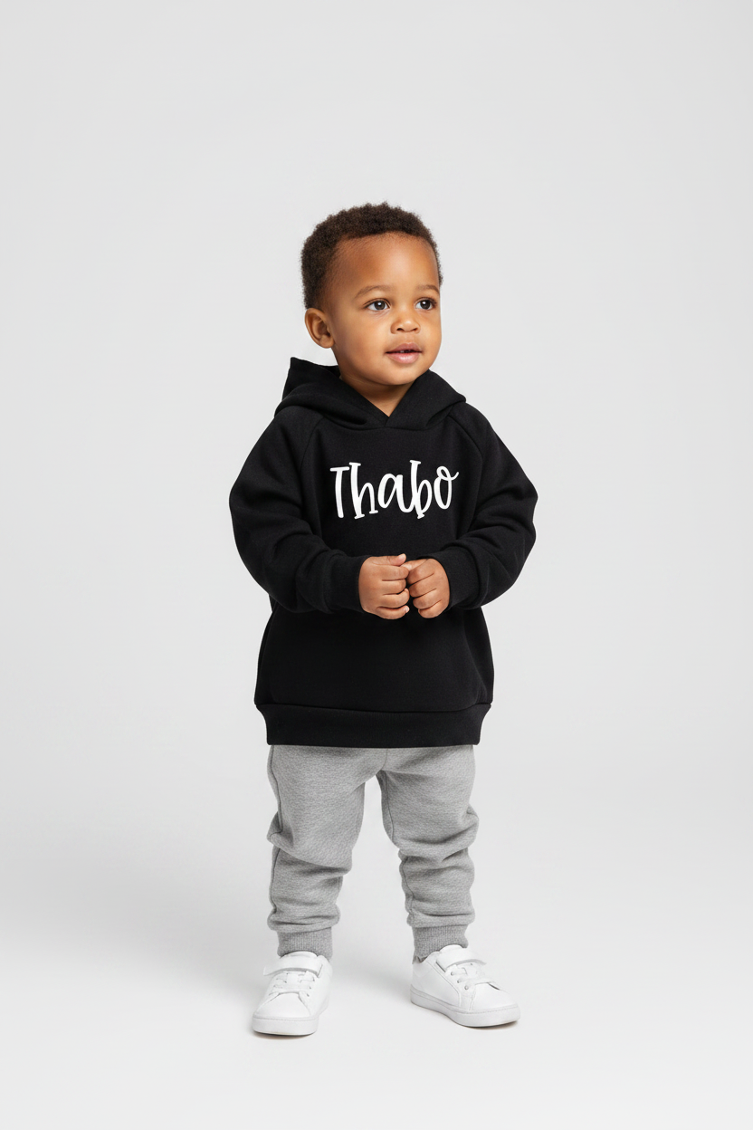 Child wearing a black hoodie with 'Thabo' printed on it, standing against a white background