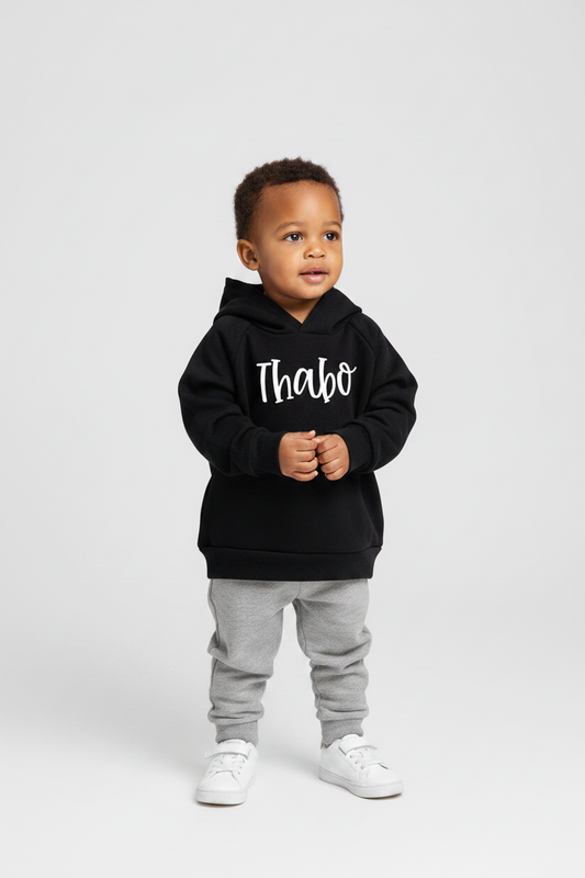 Child wearing a black hoodie with 'Thabo' printed on it, standing against a white background