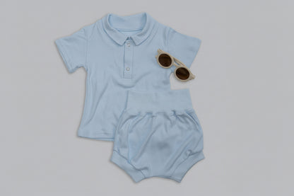 Light blue baby outfit with shorts, sippy cup, and sunglasses on a gray background