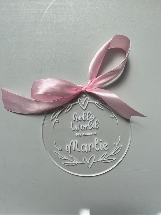 Clear circular plaque with 'hello World, My name is Marlie' text and a pink ribbon on a light gray background