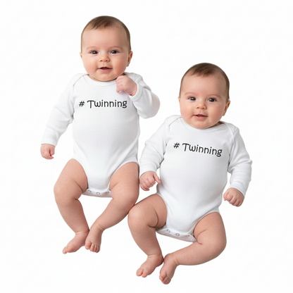 Two white baby onesies with '#Twinning' text on a white background